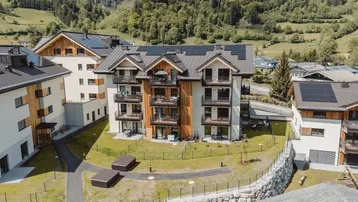 Luftaufnahme eines modernen Apartmentkomplexes mit Holzfassaden und Solaranlagen in alpiner Umgebung.