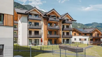 Moderne Wohnanlage mit Balkonen und Terrassen, eingebettet in eine grüne Berglandschaft.