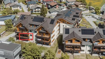 Luftaufnahme eines modernen Wohnkomplexes mit Solarpaneelen auf den Dächern und Balkonen in grüner Umgebung.