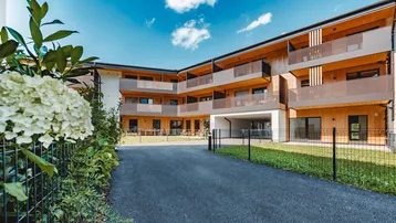 Moderne Neubau-Wohnanlage mit Holzfassade, Balkonen und gepflegter Zufahrt unter blauem Himmel.