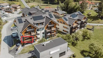 Luftaufnahme eines modernen Wohnkomplexes mit Balkonen und Solaranlagen auf den Dächern, umgeben von viel Grün.