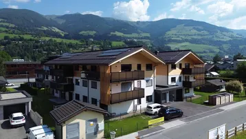 Moderne Wohnanlage mit Holzfassade, Balkonen und Photovoltaikanlage in alpiner Umgebung.