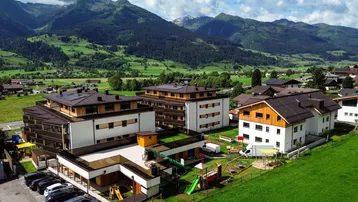 Moderne Wohngebäude mit Photovoltaikanlagen und Kinderspielplatz vor einer beeindruckenden Bergkulisse.