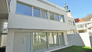 Moderne Neubauwohnung mit großzügigen Glasfronten und direktem Zugang zu einer kleinen Rasenfläche.