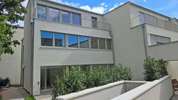 Moderne Wohnanlage mit heller Fassade, großen Fenstern und Zugang zum Gartenbereich.