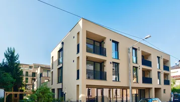 Modernes Mehrfamilienhaus mit beigefarbener Fassade, großen Fenstern und Balkonen an einem sonnigen Tag.