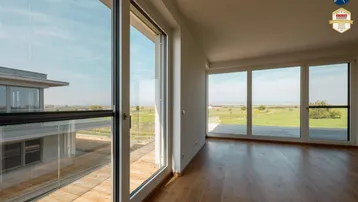 Lichtdurchflutetes Wohnzimmer mit weitem Blick über die grüne Landschaft durch bodentiefe Fenster.