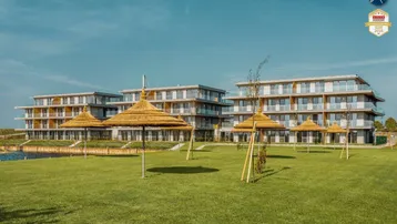 Moderne Wohngebäude am Seeufer mit weitläufiger Rasenfläche und Strohschirmen für entspannte Stunden.