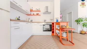 Moderne Küche mit weißen Hochglanzschränken, Holzarbeitsplatte und einem auffälligen orangefarbenen Servierwagen.