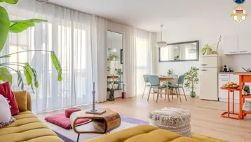 Helles, offenes Wohn- und Esszimmer mit farbenfroher Einrichtung, Holzboden und großen Fenstern.