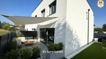 Moderne Hausfassade mit großer, möblierter Terrasse und Sonnensegel, umgeben von Grünflächen.