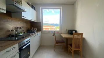 Helle Küche mit weißen Schränken, Holzarbeitsplatte und einem kleinen Essbereich am Fenster mit Ausblick.