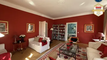 Geräumiges Wohnzimmer mit roten Wänden, Holzboden, Stuckdecke und gemütlichen Sofas.