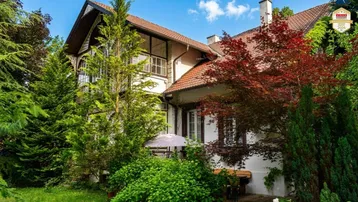 Historisches Gebäude mit üppigem Garten und traditioneller Architektur unter blauem Himmel.
