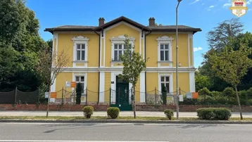 Gelbes historisches Gebäude mit weißen Fenstern und grüner Eingangstür, von der Straße aus gesehen.