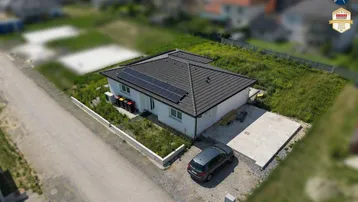Luftaufnahme eines modernen Einfamilienhauses mit Solaranlage auf dem Dach und umliegendem Grundstück.