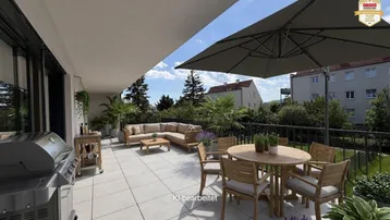 Geräumige Terrasse mit modernen Fliesen, bequemen Gartenmöbeln, Grillbereich und Sonnenschirm.