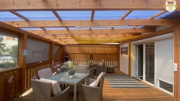 Große, überdachte Holzterrasse mit bequemen Gartenmöbeln, ideal für entspannte Stunden im Freien.