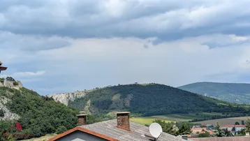 Weitläufiger Blick über hügelige Landschaft und Dächer, mit bewölktem Himmel.