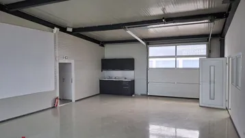 Geräumiger Gewerberaum mit hoher Decke, Betonboden und integrierter Küchenzeile, ideal für Werkstatt oder Lager.