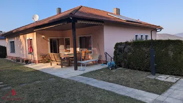 Gemütliche Terrasse am Haus mit Gartenmöbeln, umgeben von Rasen und Hecken.