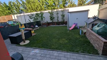 Gepflegter Gartenbereich mit Rasenfläche, Spielgeräten und einem Gartenhaus.