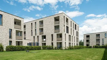 Moderne Mehrfamilienhäuser mit heller Klinkerfassade und gepflegten Grünflächen unter blauem Himmel.