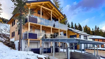 Modernes Holzhaus mit mehreren Balkonen, Carport und Photovoltaikanlage in verschneiter Berglandschaft.