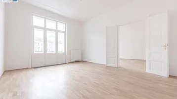 Helles, leeres Zimmer mit hohen Decken, großen Fenstern und hellem Parkettboden, bereit zur Einrichtung.