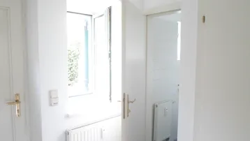 Heller Flurbereich mit offenem Fenster und Zugang zu einem gefliesten Badezimmer.
