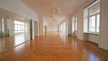 Großer, heller Raum mit Fischgrätparkett, hohen Decken und Spiegelfront an einer Wand.