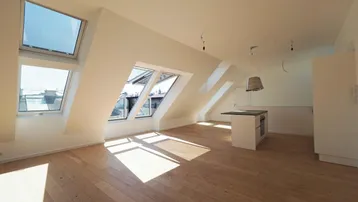 Helles Dachgeschosszimmer mit Holzboden, Dachfenstern und einem Küchenblock.