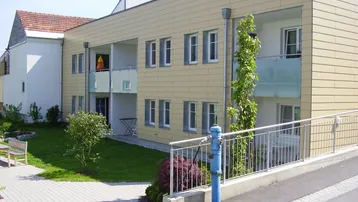 Modernes Mehrfamilienhaus mit hellbeiger Fassade, Balkonen und gepflegter Grünanlage.