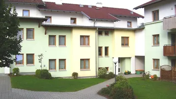 Mehrfamilienhaus mit farbiger Fassade, gepflegtem Vorgarten und Zugang zum Innenhof.