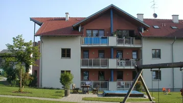 Mehrfamilienhaus mit roten Ziegeldächern, Balkonen und einem Spielplatz im gepflegten Gartenbereich.