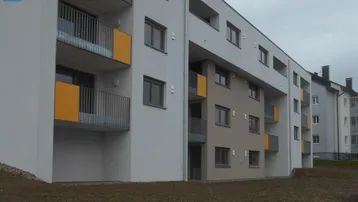 Modernes Mehrfamilienhaus mit Balkonen und farbigen Akzenten an der Fassade, umgeben von Grünflächen.