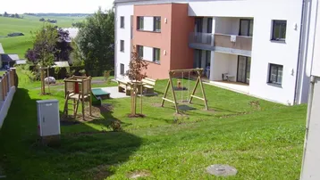 Modernes Mehrfamilienhaus mit Photovoltaikanlage, Balkonen und einem Spielplatz im Grünen.