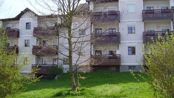 Mehrfamilienhaus mit mehreren Balkonen und einer grünen Rasenfläche im Vordergrund unter blauem Himmel.