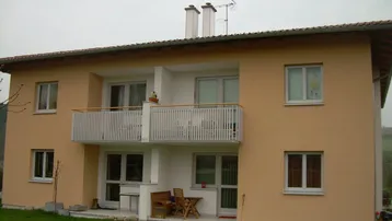 Zweifamilienhaus mit beigefarbener Fassade, Balkon im Obergeschoss und Terrasse im Erdgeschoss.