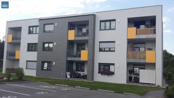 Modernes Mehrfamilienhaus mit Balkonen, grauer Fassadenverkleidung und Parkplätzen im Vordergrund.