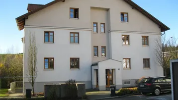 Mehrfamilienhaus mit heller Fassade, braunen Fenstern und gepflegter Umgebung in einer Wohngegend.