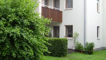 Gepflegte Gebäudefassade mit Balkonen und einem grünen Vorgartenbereich.