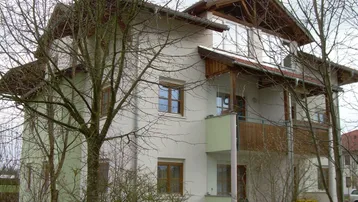 Mehrfamilienhaus mit moderner Architektur, Balkonen und gepflegter Fassade umgeben von Bäumen.