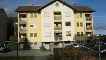 Mehrfamilienhaus mit gelber und weißer Fassade, mehreren Balkonen und Außenparkplätzen.