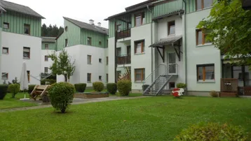 Mehrere Wohngebäude mit grünen Fassaden und einem gepflegten Gemeinschaftsgarten mit Spielbereich.