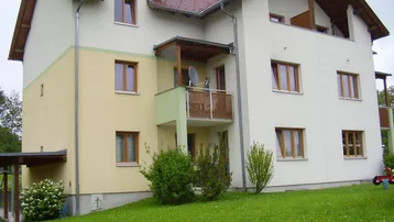 Mehrfamilienhaus mit Satteldach, Balkon und gepflegtem Gartenbereich in grüner Umgebung.