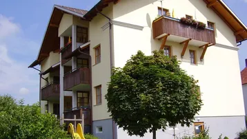 Mehrfamilienhaus mit mehreren Balkonen, Satteldach und einem Spielbereich mit Rutsche im Garten.