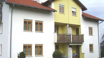Gepflegtes Mehrfamilienhaus mit weißer und gelber Fassade, roten Ziegeldächern und Balkonen.