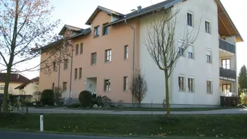 Mehrfamilienhaus mit heller Fassade, Satteldach und Balkonen in grüner Umgebung.