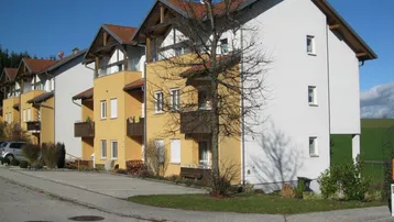 Mehrfamilienhaus mit weißer und gelber Fassade in ländlicher Umgebung unter blauem Himmel.